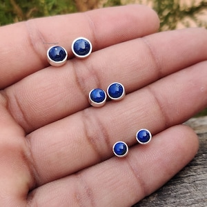 May include: A set of four silver stud earrings with round blue lapis lazuli gemstones.