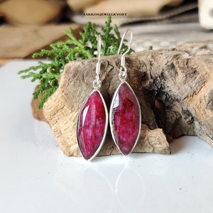 May include: A pair of silver dangle earrings with red gemstone drops. The earrings have a marquise shape and are set in a silver bezel.