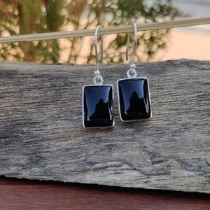 May include: A pair of silver dangle earrings with black rectangular gemstones.