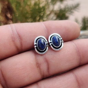 Puede incluir: Un par de pendientes de plata con piedras ovaladas de lapislázuli. Las piedras son de color azul intenso con motas doradas.