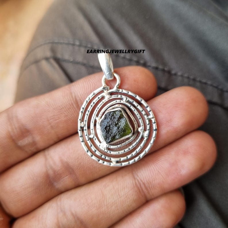 May include: A silver pendant with a green gemstone set in a circular design with concentric circles.