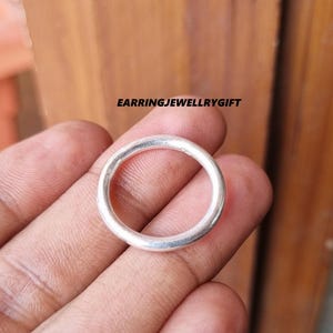 May include: A simple silver ring, shown on a hand, with a smooth, rounded surface.