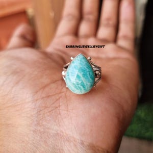 May include: A silver ring with a teardrop-shaped green gemstone. The ring has a delicate design with small silver beads and a textured band.