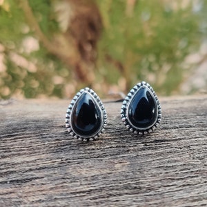 Puede incluir: Un par de pendientes de plata en forma de lágrima con detalles de piedras preciosas negras.