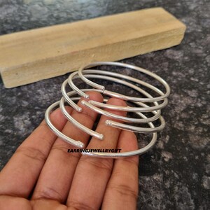 May include: Five silver bangles stacked on top of each other. The bangles are simple and have a smooth, polished finish.