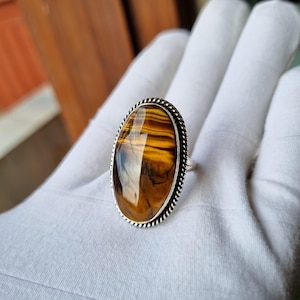 May include: A silver ring featuring an oval tiger's eye gemstone. The gemstone displays brown and gold stripes.