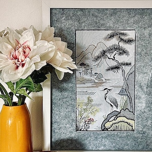 Peut inclure: Une estampe en noir et blanc encadrée d'un paysage japonais avec un oiseau debout sur un rocher. L'estampe est dans un cadre blanc avec un passe-partout gris. L'estampe est sur une surface blanche avec un vase de fleurs blanches et un rocher.