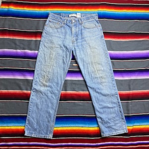 Peut inclure: Un jean en denim bleu clair à l'aspect délavé et à la coupe droite. Le jean a une braguette à boutons et cinq poches.