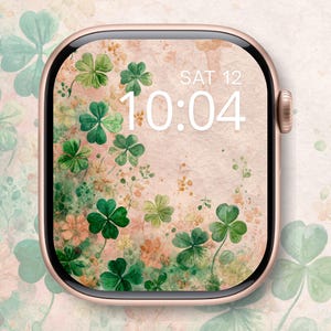 May include: A rose gold smartwatch displays a floral design with green shamrocks and delicate flowers. The screen shows the date, Saturday the 12th, and the time, 10:04, in white text. The background has a soft, watercolor-like texture.