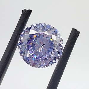 May include: A round, clear, purple gemstone with facets. The gemstone is held by two black tweezers.