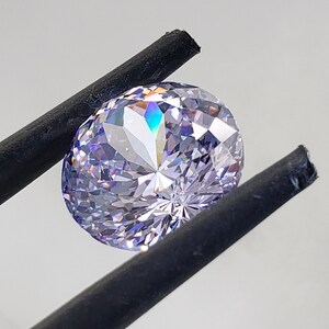 May include: A clear, round, faceted gemstone with a light purple hue. The gemstone is held by a pair of black tweezers.