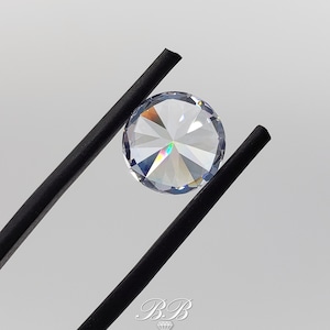 May include: A clear round gemstone with a rainbow effect, held by black tweezers.
