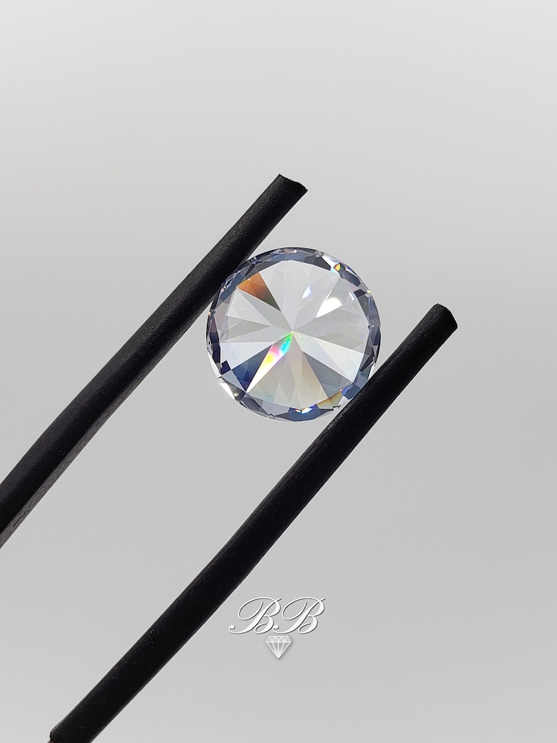 May include: A clear round gemstone with a rainbow effect, held by black tweezers.