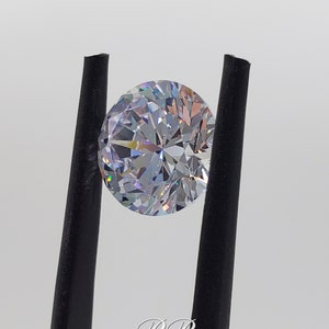 May include: A clear round gemstone with a brilliant cut, held by black tweezers. The gemstone has a rainbow-like effect.