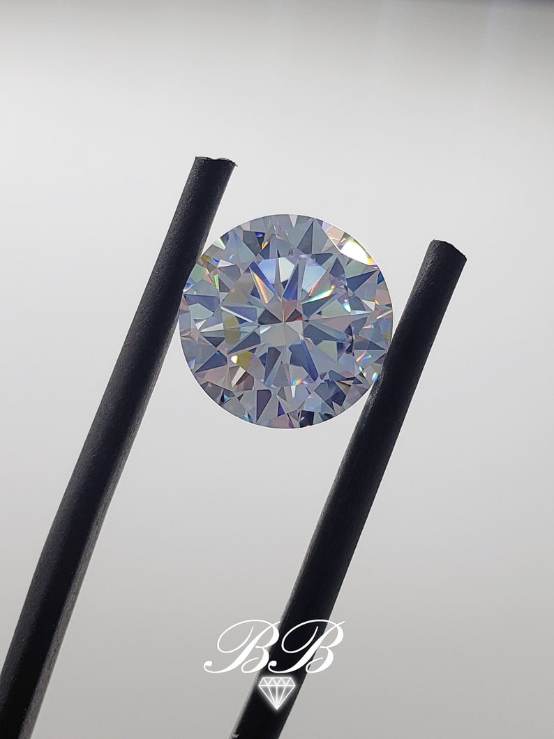 May include: A clear round gemstone with a faceted cut, held by black tweezers. The gemstone has a rainbow iridescent effect.