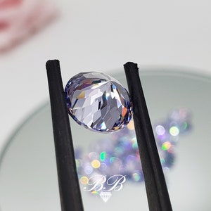 May include: A clear, faceted, oval-shaped gemstone with a light purple hue. The gemstone is held by black tweezers against a white background.