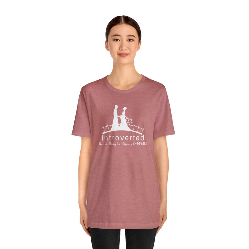 May include: A heather red t-shirt with a white graphic of a couple walking on a bridge. The graphic includes the text "Introverted but willing to discuss C-DRAMA".