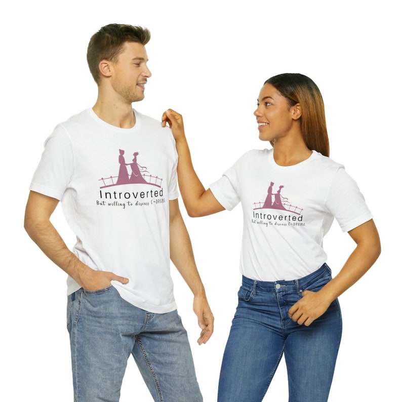 May include: Two white t-shirts with a pink graphic of a couple holding hands on a bridge. The text on the shirts reads "Introverted but willing to discuss ( -_-) /  "