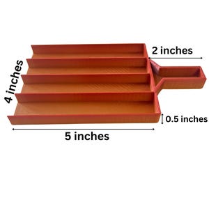 Peut inclure: Un plateau à niveaux, de couleur rouge orangé, avec une poignée. Le plateau mesure 12,7 cm de long, 10,2 cm de large et 5,1 cm de haut. La poignée mesure 1,3 cm de large. Le plateau a quatre niveaux.