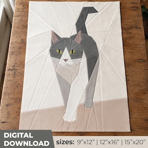 May include: A geometric fabric wall hanging featuring a stylised cat in shades of grey, white, and tan with yellow eyes. The design is composed of angular fabric segments. Text at the bottom reads: DIGITAL DOWNLOAD sizes: 9"x12" | 12"x16" | 15"x20".