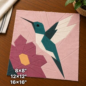 Può includere: Un blocco di tessuto quadrato per trapunte con un colibrì realizzato in pezzi di colore verde acqua e bianco, sospeso sopra un fiore rosa scuro con centro giallo, su sfondo rosa chiaro. Il testo indica le dimensioni 8x8, 12x12 e 16x16 pollici.