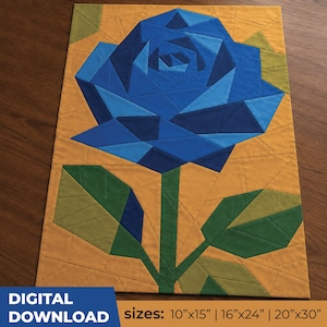 May include: A rectangular quilt pattern featuring a large blue rose composed of geometric fabric segments in various shades of blue. The rose has a green stem and two green leaves against a mustard yellow background. Text states: DIGITAL DOWNLOAD sizes: 10"x15" | 16"x24" | 20"x30".