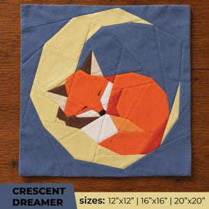 May include: A square fabric quilt block featuring a geometric paper-pieced design of a sleeping orange fox curled inside a pale yellow crescent moon, set against a dark blue background. The text reads CRESCENT DREAMER sizes: 12"x12" | 16"x16" | 20"x20".