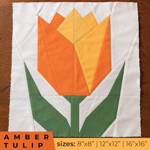 May include: A fabric quilt block featuring a geometric tulip design in shades of orange and yellow with green leaves on a white background. The text AMBER TULIP and sizes 8"x8" | 12"x12" | 16"x16" are printed at the bottom of the image.