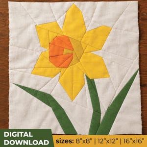 May include: A square fabric quilt block featuring a pieced daffodil design with yellow petals, an orange center, and green leaves on a white background. The text at the bottom reads DIGITAL DOWNLOAD sizes: 8"x8" | 12"x12" | 16"x16".