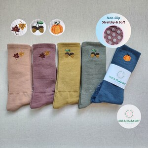 May include: Five pairs of colorful socks with embroidered autumn-themed designs, including leaves, acorns, and pumpkins. The socks are non-slip and stretchy, with a polka dot pattern on the bottom. The socks are packaged with a white label that says "SUE & Market ART".