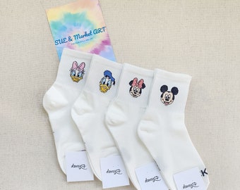 Może przedstawiać: Cztery pary białych skarpet do kostek z wzorami postaci z Disneya. Skarpety przedstawiają Myszki Miki, Minnie Mouse, Donalda Ducka i Daisy Duck. Każda skarpeta ma małą metkę z logo Disneya.