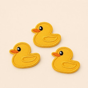 Peut inclure: Trois écussons brodés en forme de canard jaune. Chaque écusson présente un corps jaune vif, un petit bec orange et un œil noir et blanc. La broderie est dense avec une bordure définie, créant un aspect plat et uniforme pour chaque canard.