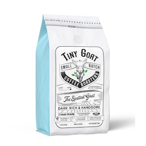 May include: A white bag of coffee beans with a blue border. The bag features a logo with a cartoon goat and the text "Tiny Goat Small Batch Coffee Roasters". The text "The Spotted Goat" is printed in black on a white background. The bag also includes the text "Dark, Rich & Handsome" and "Fair Trade".