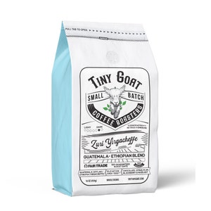 May include: A white and light blue bag of Tiny Goat Small Batch Coffee Roasters whole beans. The bag features a goat illustration and text that reads "Zuri Yirgacheffe, Guatemala-Ethiopian Blend." The bag contains 16 oz (454g) of coffee.
