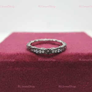 May include: A silver band ring with a delicate design and small clear stones set in the band.