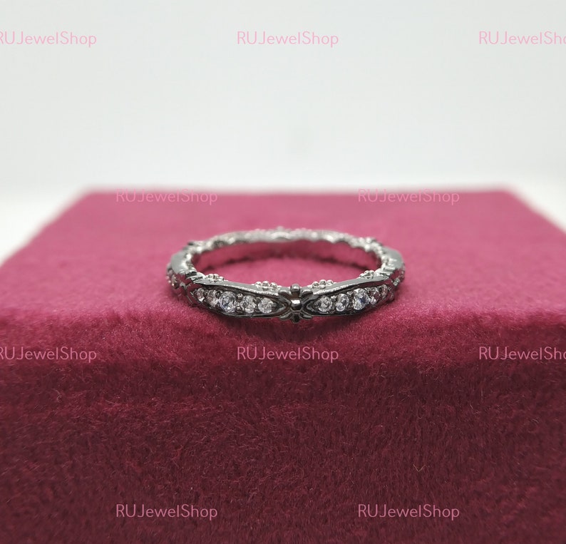May include: A silver band ring with a delicate design and small clear stones set in the band.