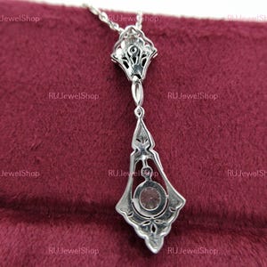 May include: A silver pendant necklace with a large, clear gemstone in the center. The pendant is intricately designed with a floral pattern and has a delicate chain.