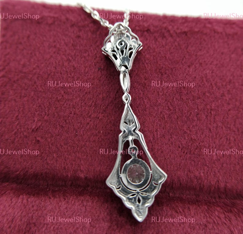 May include: A silver pendant necklace with a large, clear gemstone in the center. The pendant is intricately designed with a floral pattern and has a delicate chain.