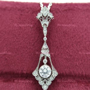 May include: A silver pendant necklace with a large, round, clear gemstone surrounded by smaller clear gemstones. The pendant is in an ornate, Art Deco style with intricate details.