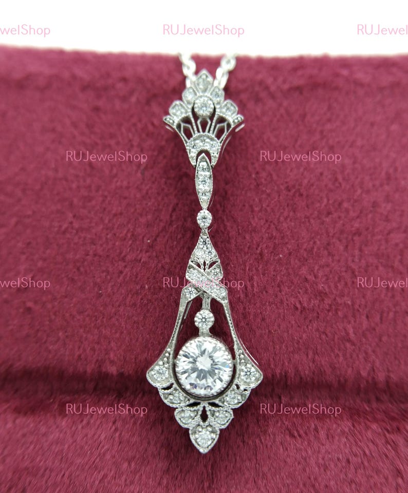 May include: A silver pendant necklace with a large, round, clear gemstone surrounded by smaller clear gemstones. The pendant is in an ornate, Art Deco style with intricate details.