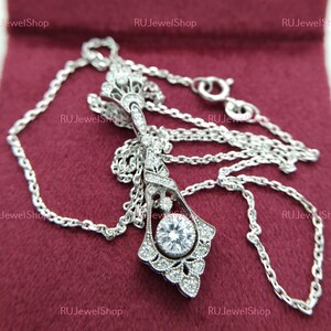 May include: A silver necklace with a delicate chain and a pendant featuring a large round stone surrounded by smaller stones in a floral design.