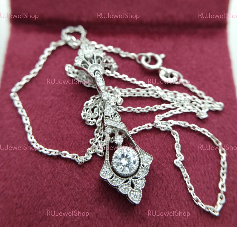 May include: A silver necklace with a delicate chain and a pendant featuring a large round stone surrounded by smaller stones in a floral design.
