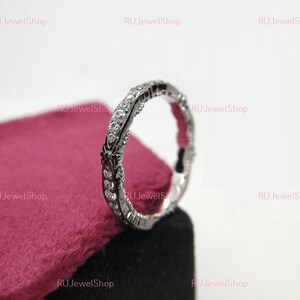 May include: A silver ring with a delicate design and small clear stones. The ring is on a red velvet background.