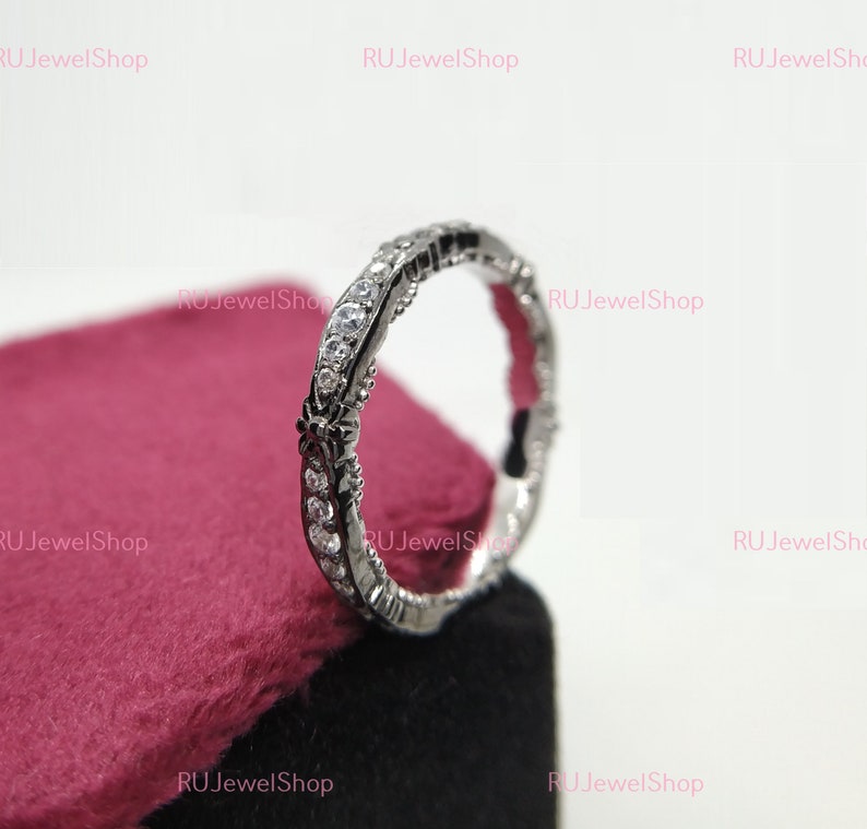 May include: A silver ring with a delicate design and small clear stones. The ring is on a red velvet background.