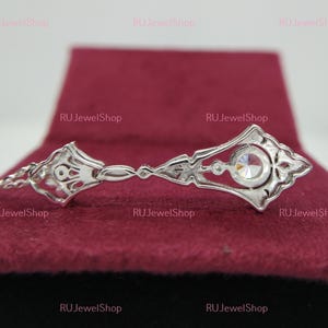 May include: A silver pendant with a clear crystal stone in the center. The pendant is in the shape of a key with intricate details. The pendant is on a red velvet background.