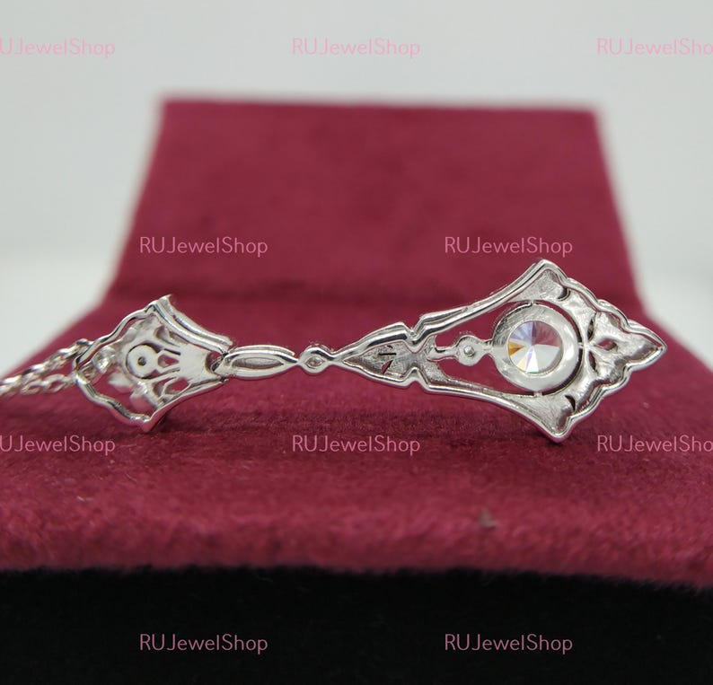 May include: A silver pendant with a clear crystal stone in the center. The pendant is in the shape of a key with intricate details. The pendant is on a red velvet background.
