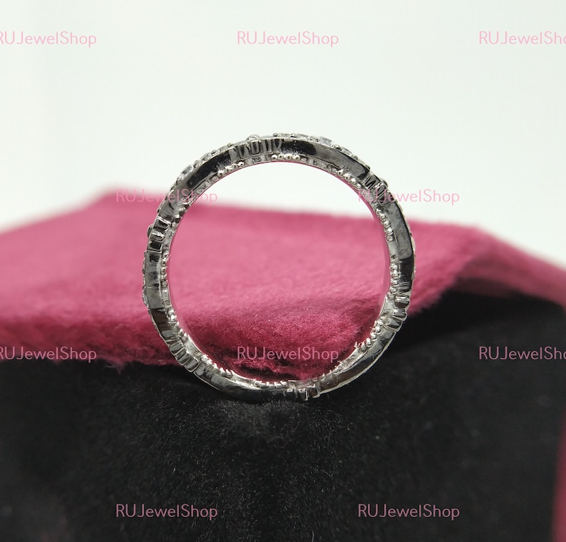 May include: A silver band ring with a row of small diamonds set in the band. The ring is on a pink velvet surface.