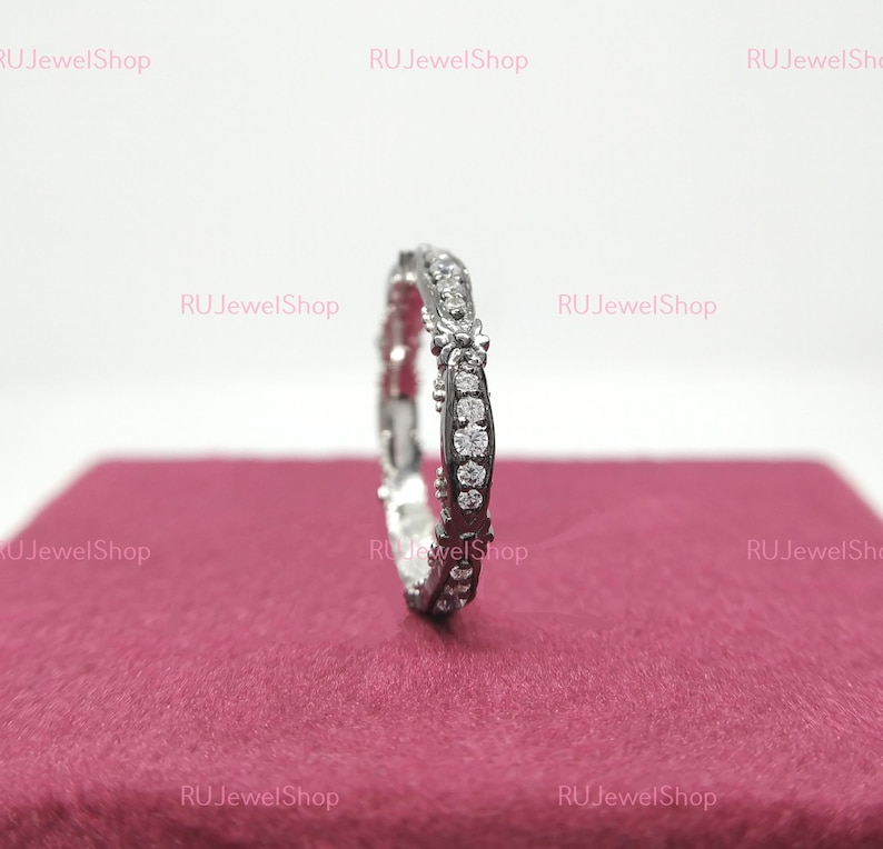 May include: A silver band ring with a row of small, clear diamonds set in a delicate, intricate design.