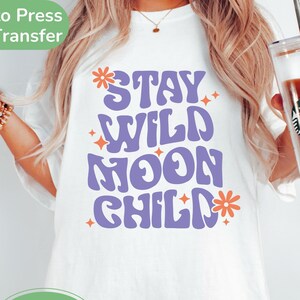 May include: White t-shirt with a purple and orange graphic that says "Stay Wild Moon Child".