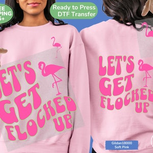 May include: Pink sweatshirt with the text "Let's Get Flocked Up" in a retro font with a pink flamingo graphic. The text is outlined in green.